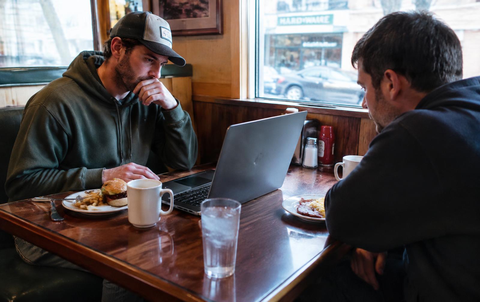 Two guys at a diner booth with a laptop between plates